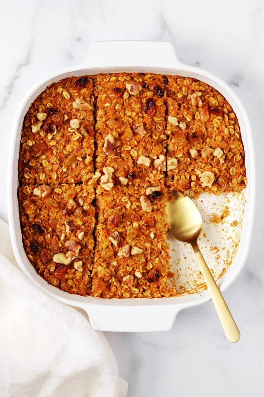 White baking dish with carrot cake baked oatmeal and a gold serving spoon