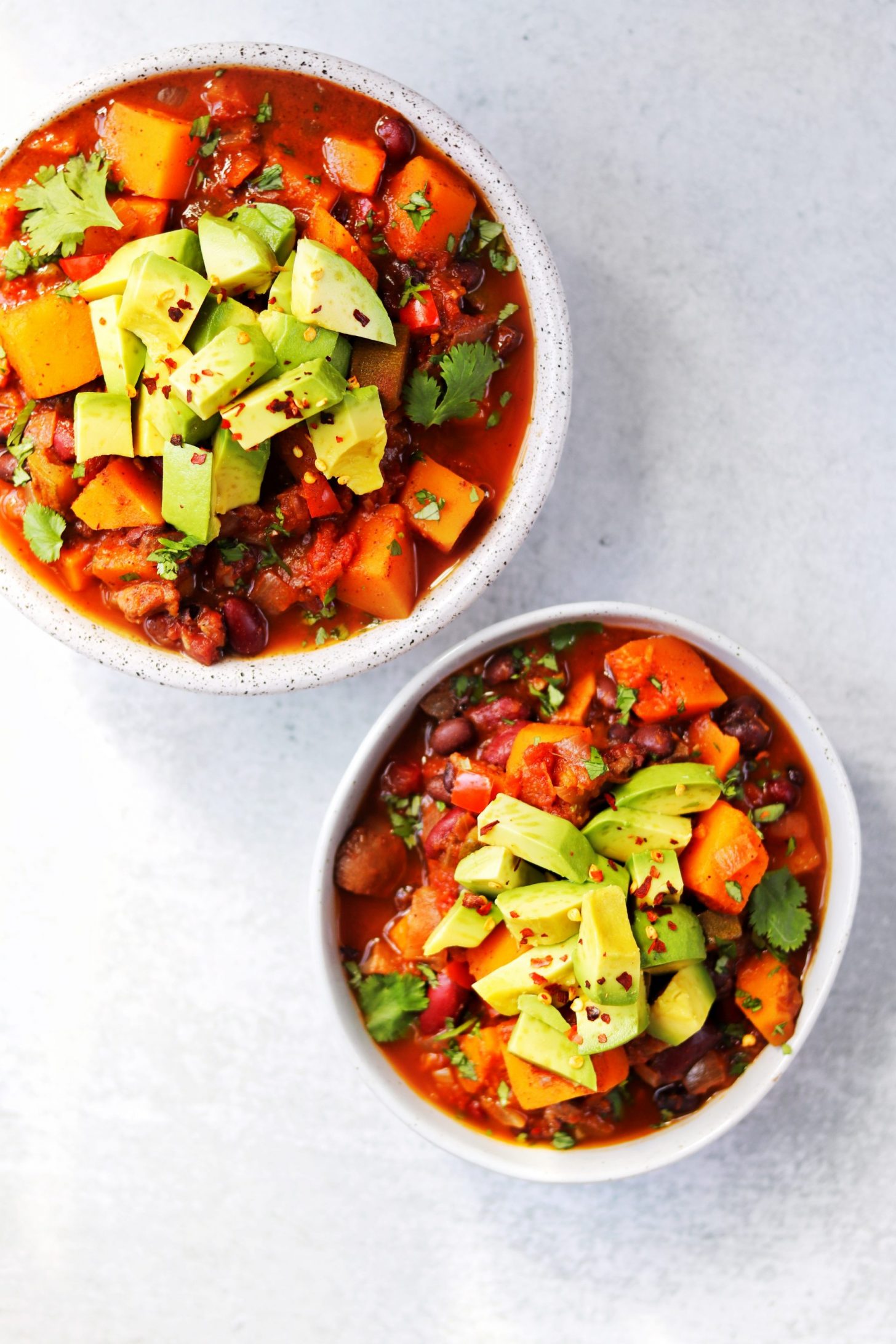 Two bowls of butternut squash black bean chili topped with avocado