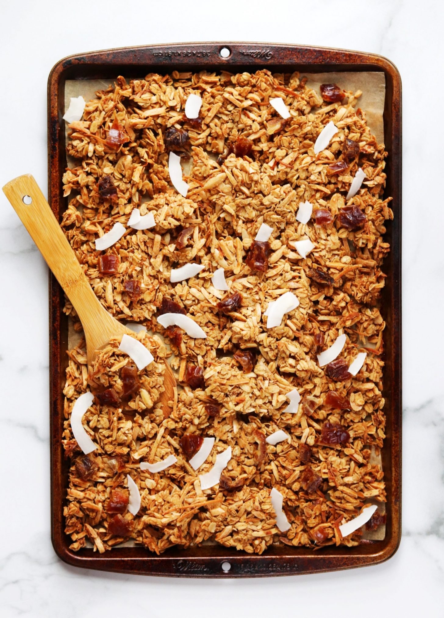 Baking tray of chai spiced granola with coconut flakes and chopped dates