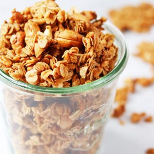 Glass jar filled with cinnamon granola on a white backdrop