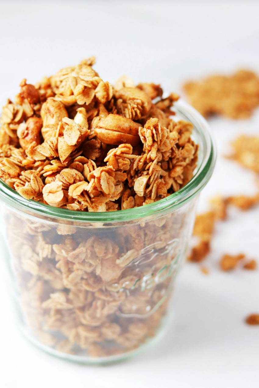 Glass jar filled with cinnamon granola on a white backdrop
