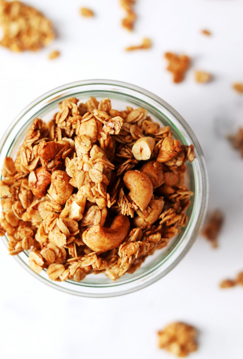 Overhead view of a jar of cinnamon crunch granola on a white backdrop with granola clusters scattered around
