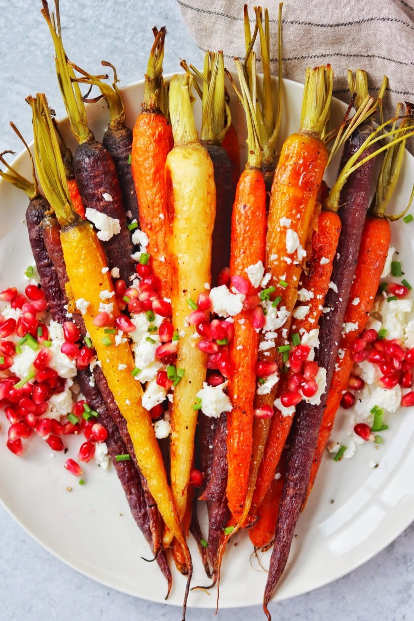 plate of roasted rainbow carrots topped with pomegranate seeds and crumbled feta 