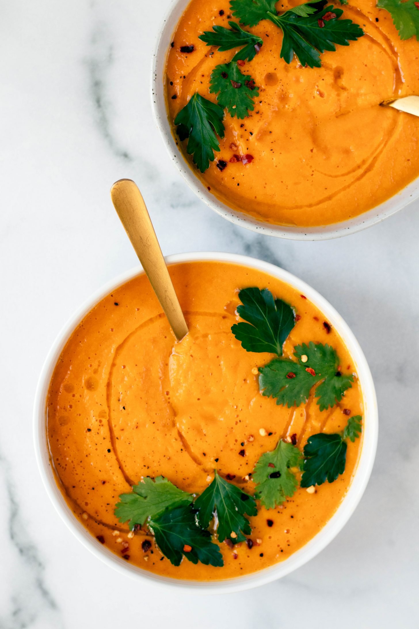 Two bowls of carrot ginger soup topped with cilantro leaves