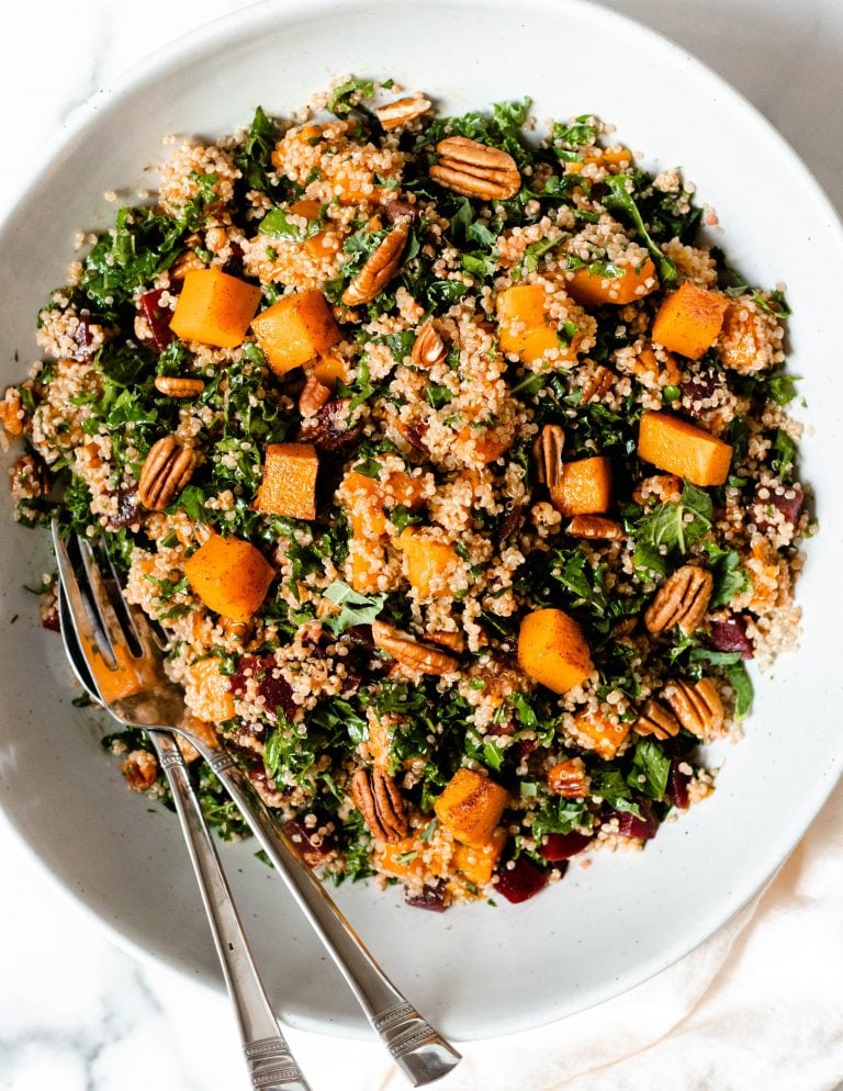 Bowl of beet quinoa salad mixed together with gold serving spoons
