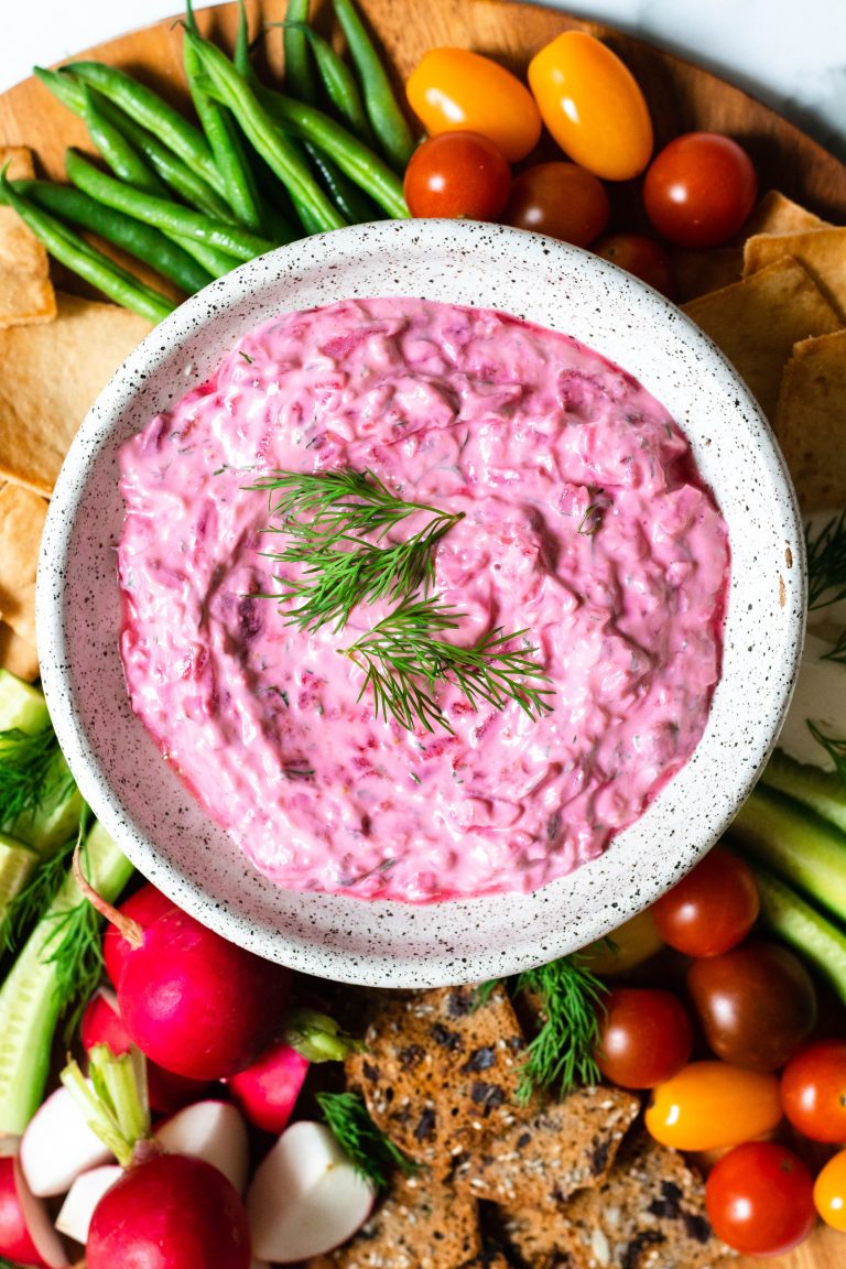 Bowl of beet tzatziki surrounded by veggie crudite and pita chips and crackers for dipping