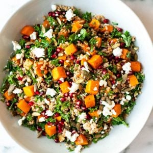 Close up of a bowl of farro salad with butternut squash,kale, pomegranate, and goat cheese