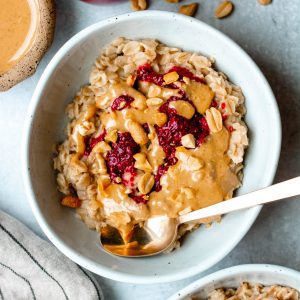 Bowl of peanut butter and jelly oatmeal with a gold spoon and bowls of ingredients