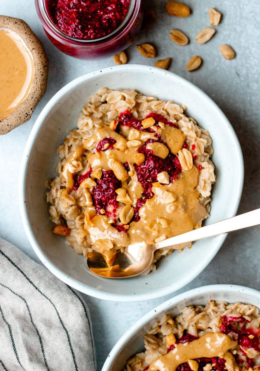 Bowl of peanut butter and jelly oatmeal with a gold spoon and small bowls of ingredients