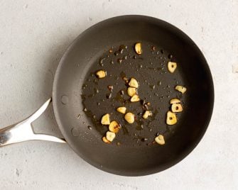 Sliced sauteed garlic in olive oil in a dark nonstick pan
