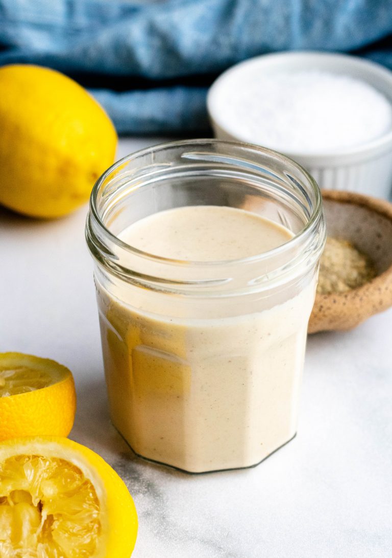 jar of lemon tahini sauce with lemons and seasonings around it