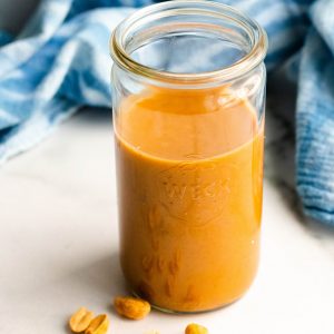healthy peanut sauce in a jar with a blue towel in the background and peanuts in the foreground