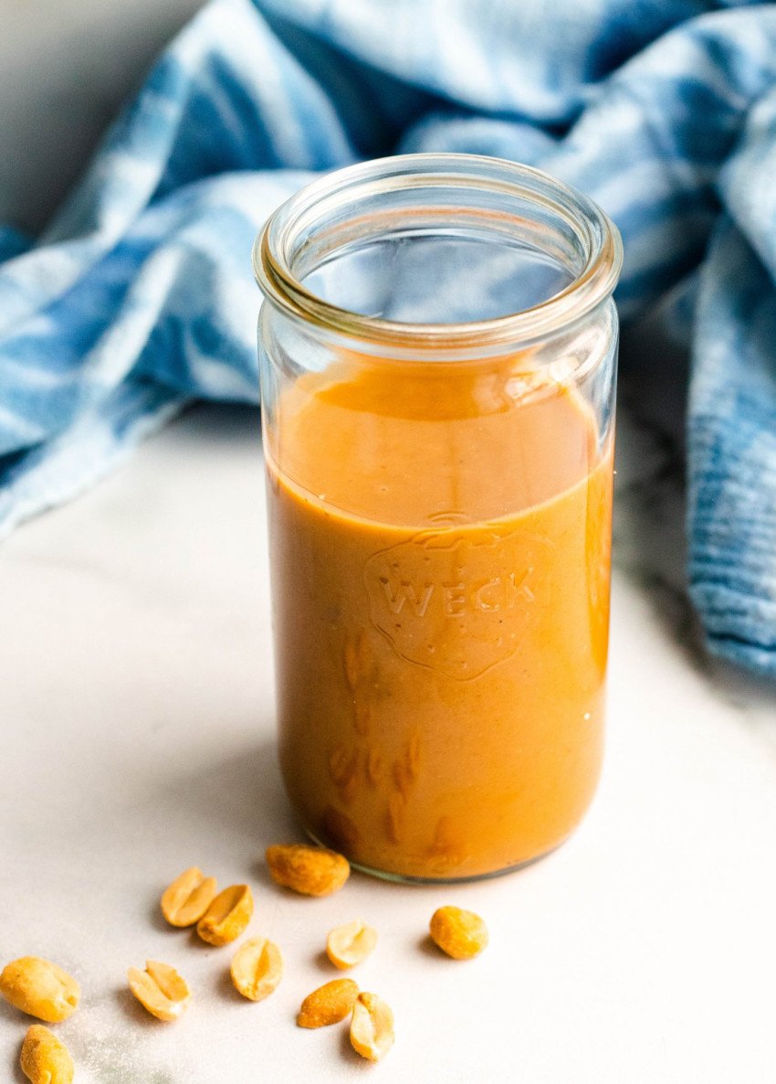 healthy peanut sauce in a jar with a blue towel in the background and peanuts in the foreground