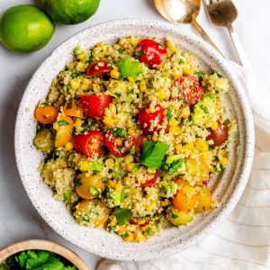 Cilantro lime quinoa salad with avocado in a bowl with ingredients around it and gold serving utensils