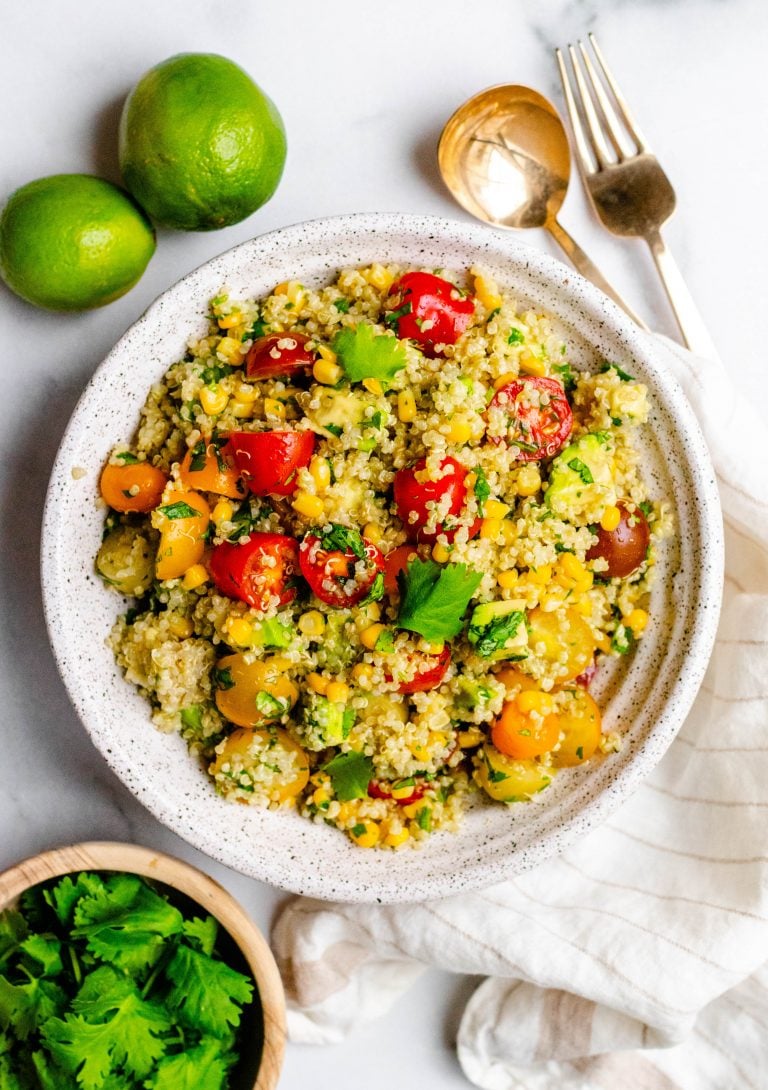 Cilantro lime quinoa salad with avocado in a bowl with ingredients around it and gold serving utensils