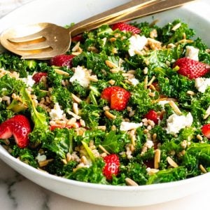 large bowl of strawberry kale salad with gold serving spoons