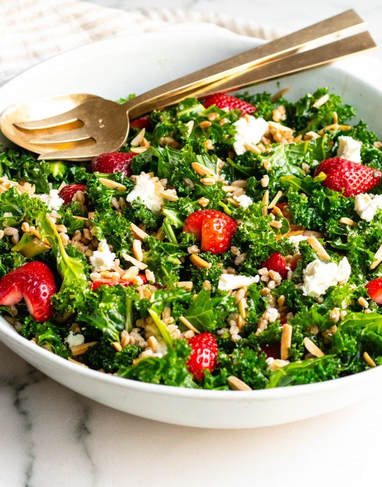 large bowl of strawberry kale salad with gold serving spoons