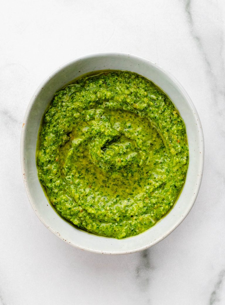 Bowl of kale pesto on a white marble backdrop