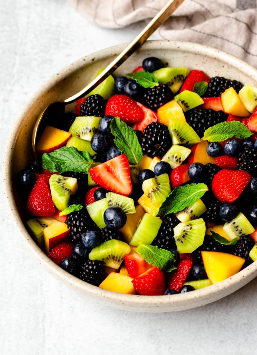 Summer fruit salad in a bowl with gold serving spoon