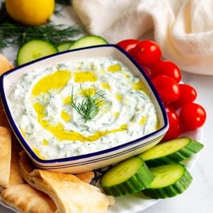 Dipping bowl with tzatziki sauce surrounded by pita and vegetables for dipping