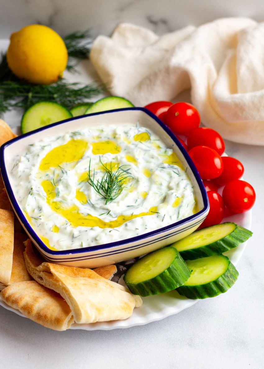 Homemade tzatziki sauce in a bowl surrounded by veggies and pita