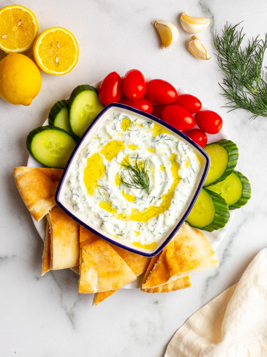 Homemade tzatziki sauce in a bowl surrounded by veggies and pita