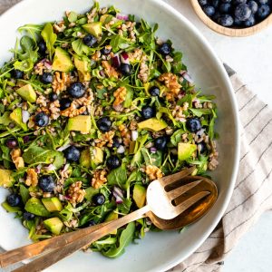 Large bowl of blueberry basil salad with gold serving spoons and a bowl of blueberries on the side