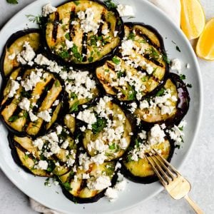 Plate of grilled eggplant slices with feta cheese and herbs with a gold serving fork