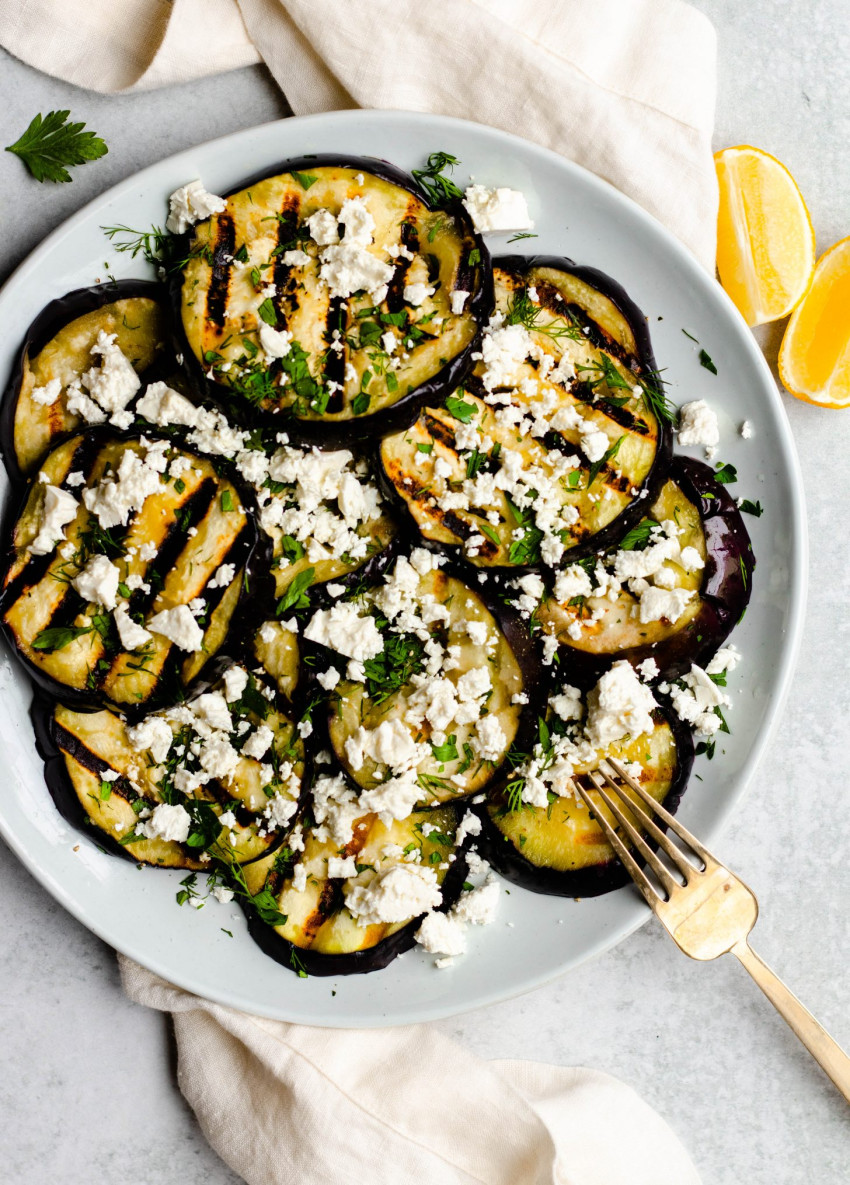 Plate of grilled eggplant slices with feta cheese and herbs with a gold serving fork
