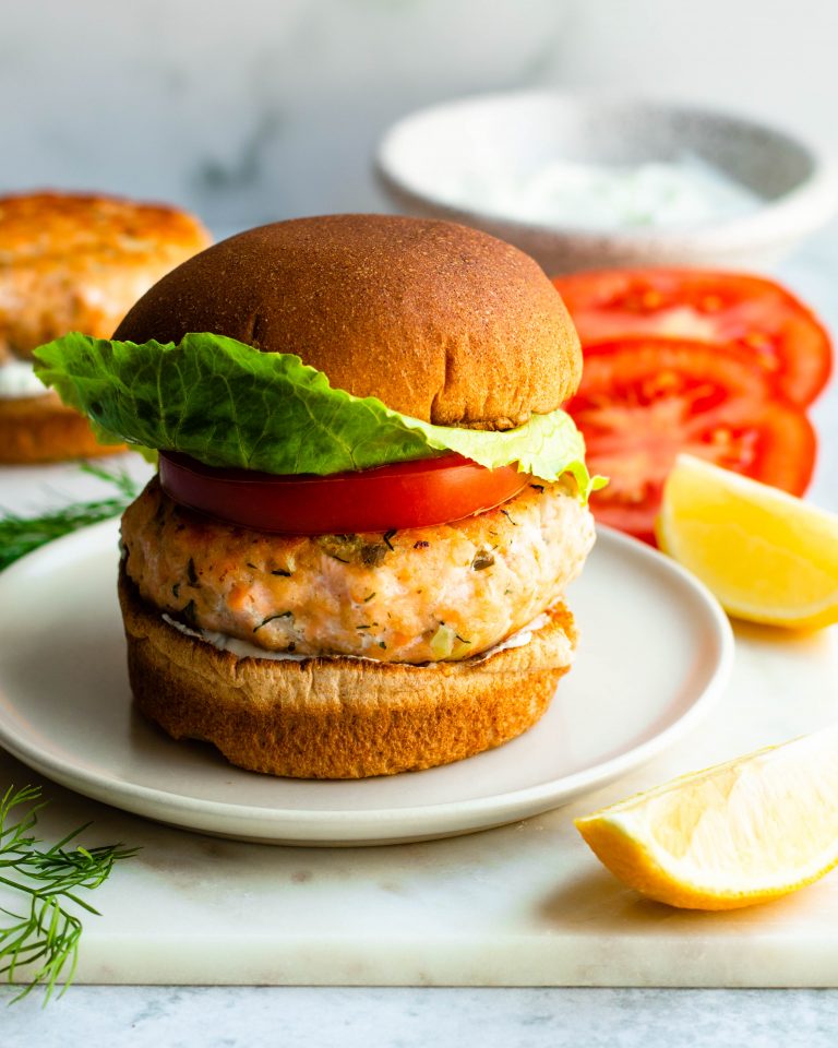 Lemon dill salmon burger on marble board surrounded by ingredients
