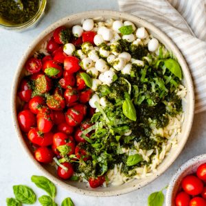 Bowl of caprese orzo salad with cherry tomatoes, basil leaves, and basil vinaigrette surrounding the bowl