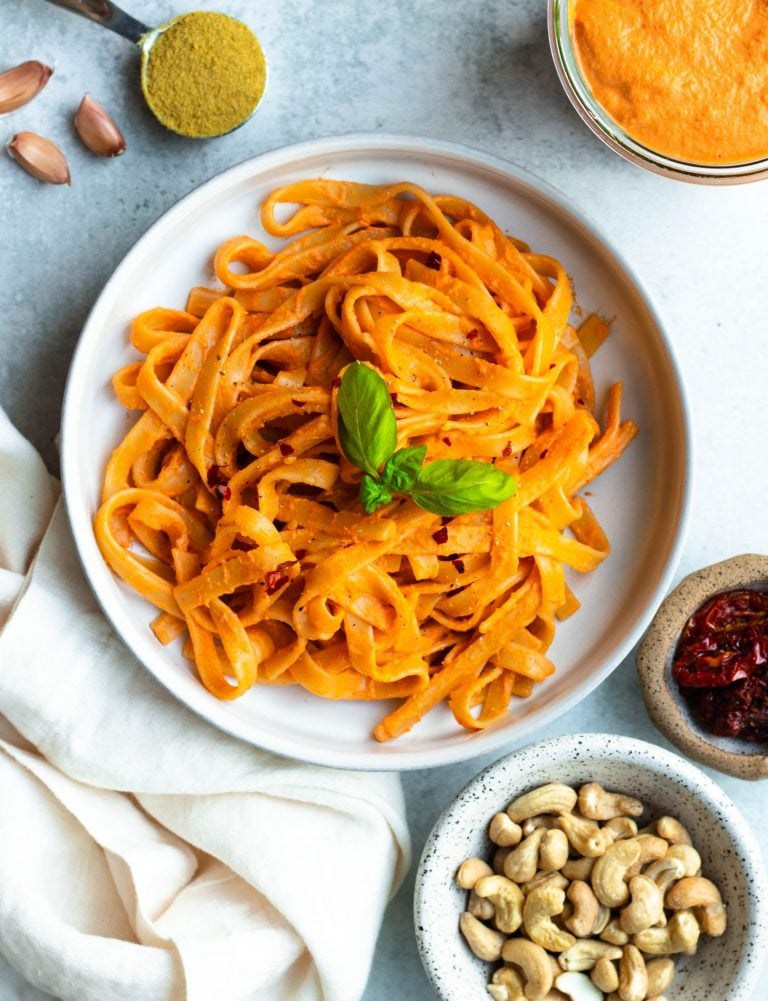 Bowl of creamy sundried tomato pasta with ingredients and sauce surrounding the bowl in small containers