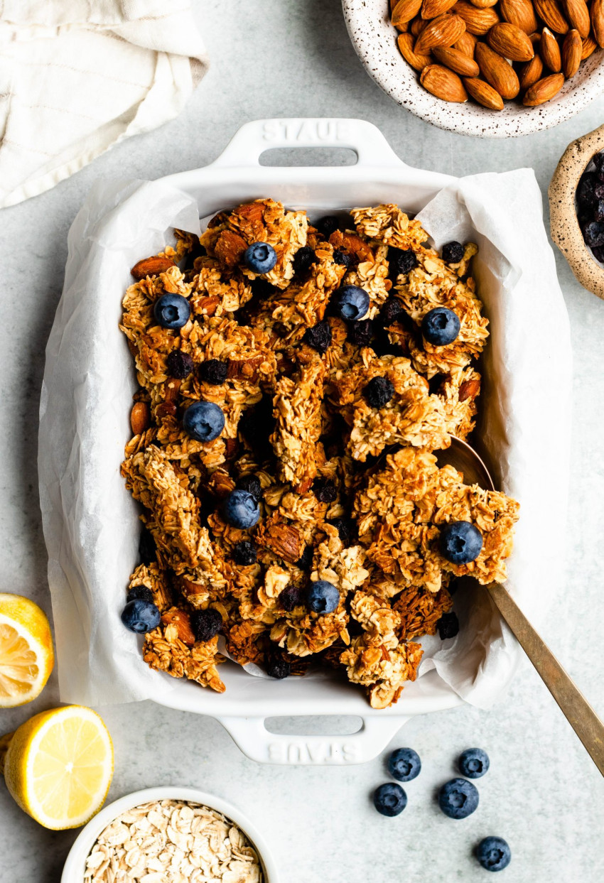 Ceramic rectangle dish filled with lemon blueberry granola, surrounded by different ingredients