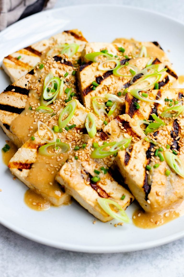 Close up of a plate of miso grilled tofu with chopped scallions, sesame seeds, and miso sesame dressing