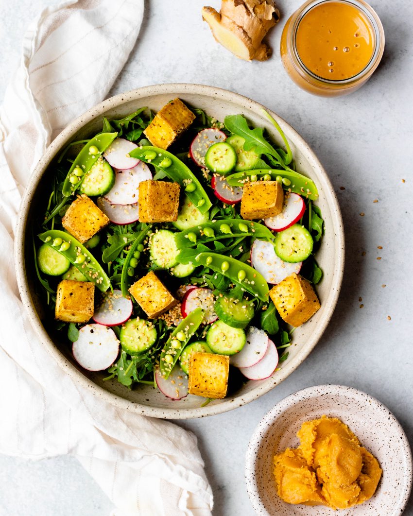 Snap pea salad next to a jar of sesame ginger miso dressing and a bowl of miso
