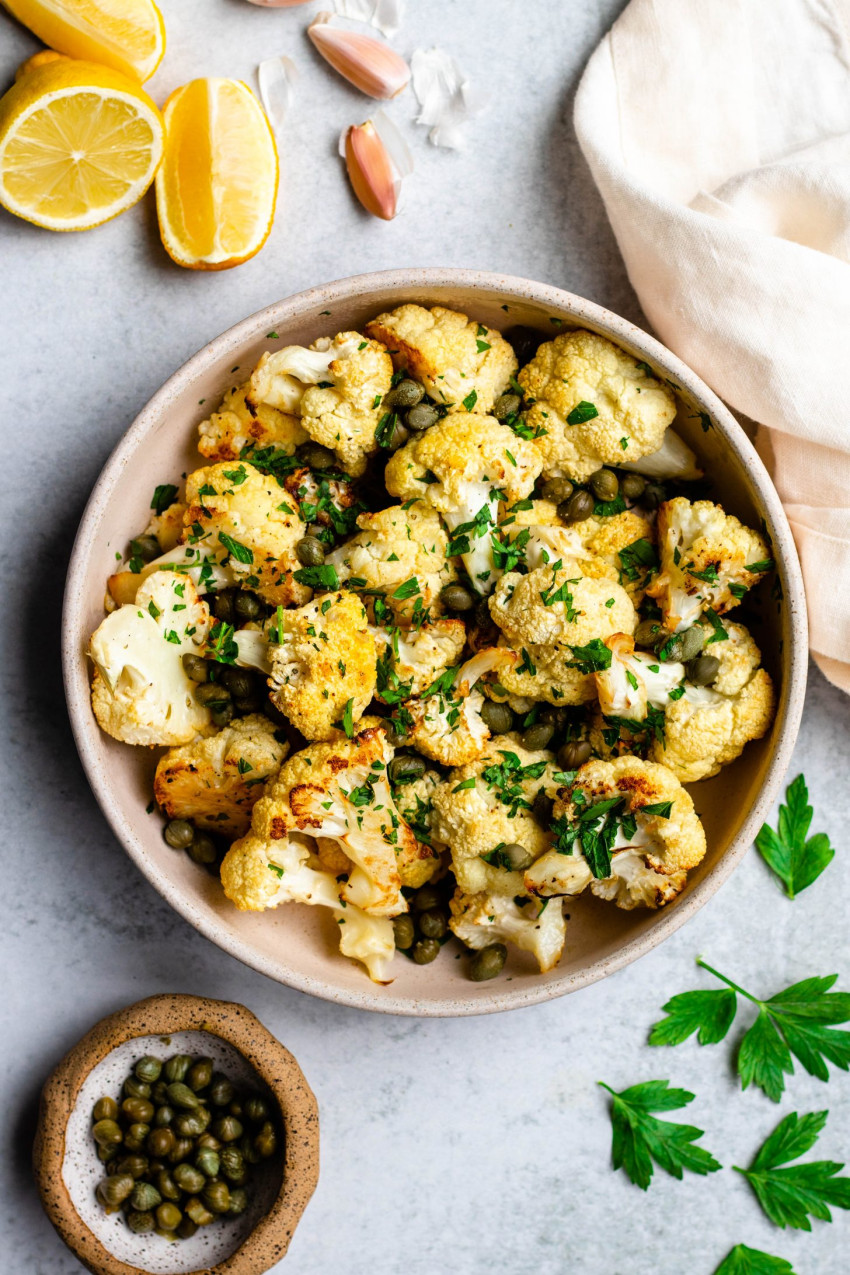 Bowl of lemon caper roasted cauliflower with ingredients surrounding the bowl