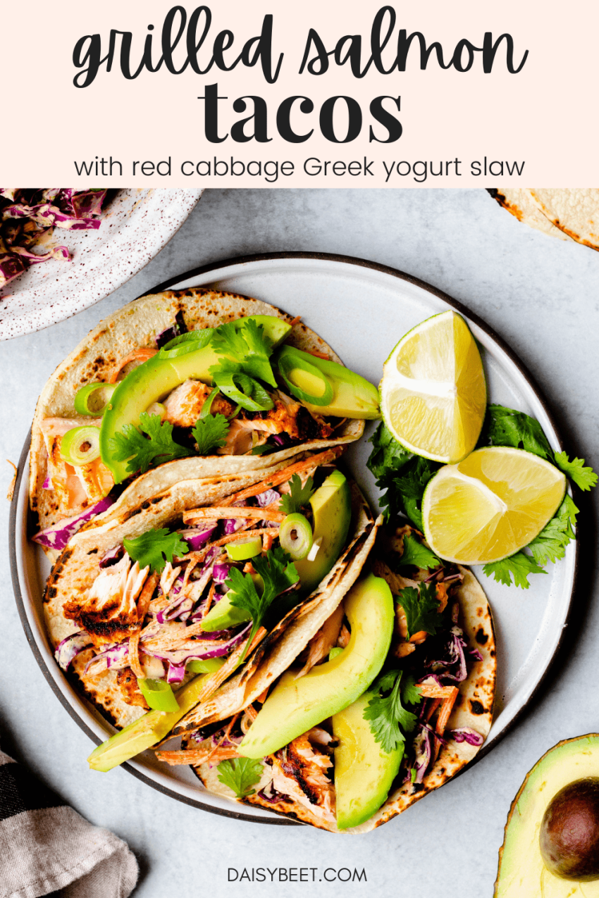 Plate of three grilled salmon tacos with red cabbage slaw with sliced avocado and limes