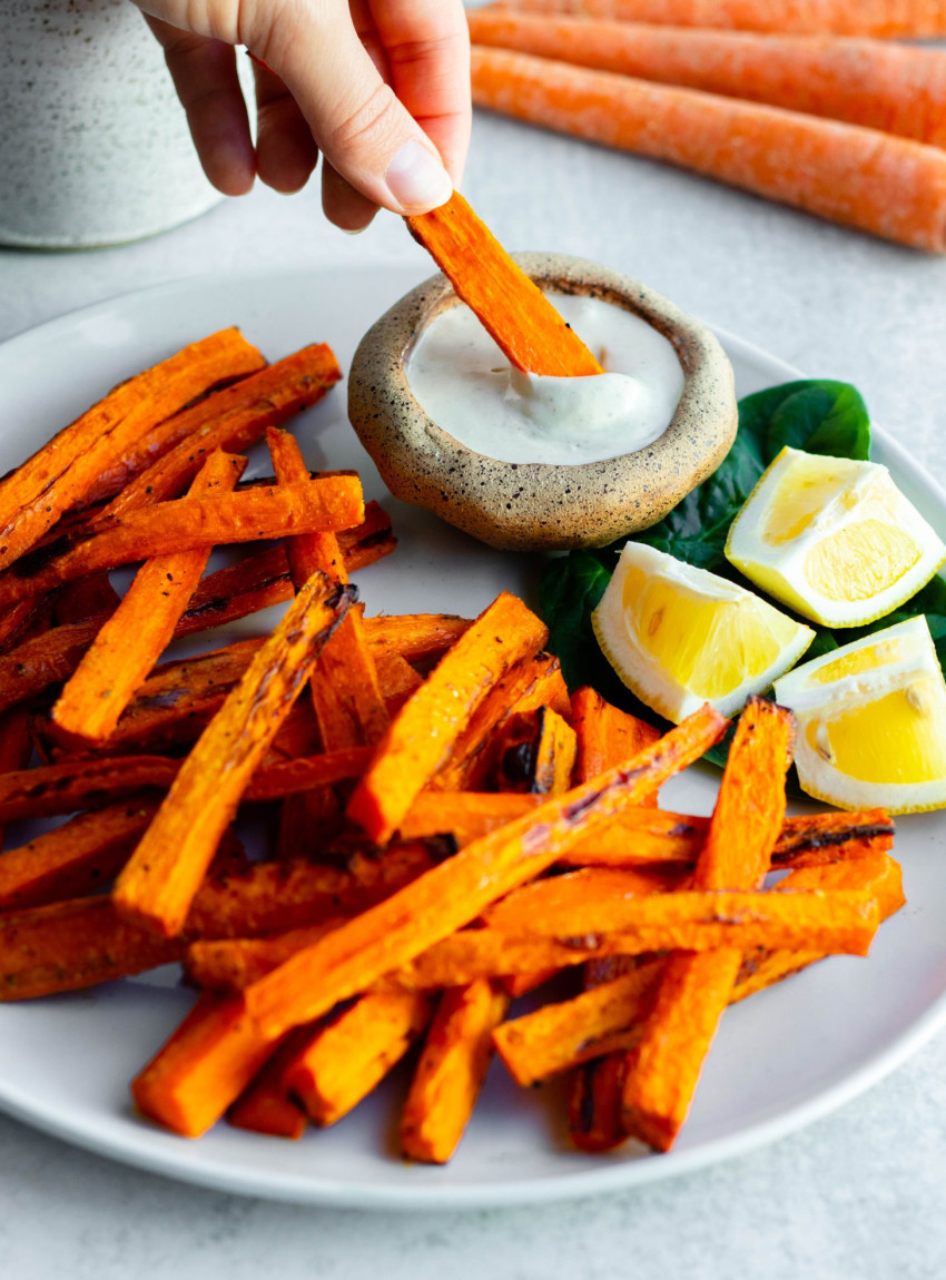 Hand dipping carrot fry into lemon tahini sauce