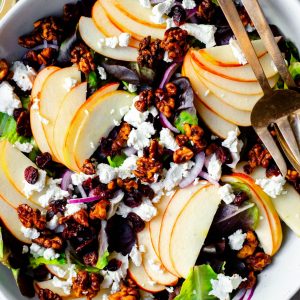 Close up of apple cranberry walnut salad in a bowl with gold serving spoons