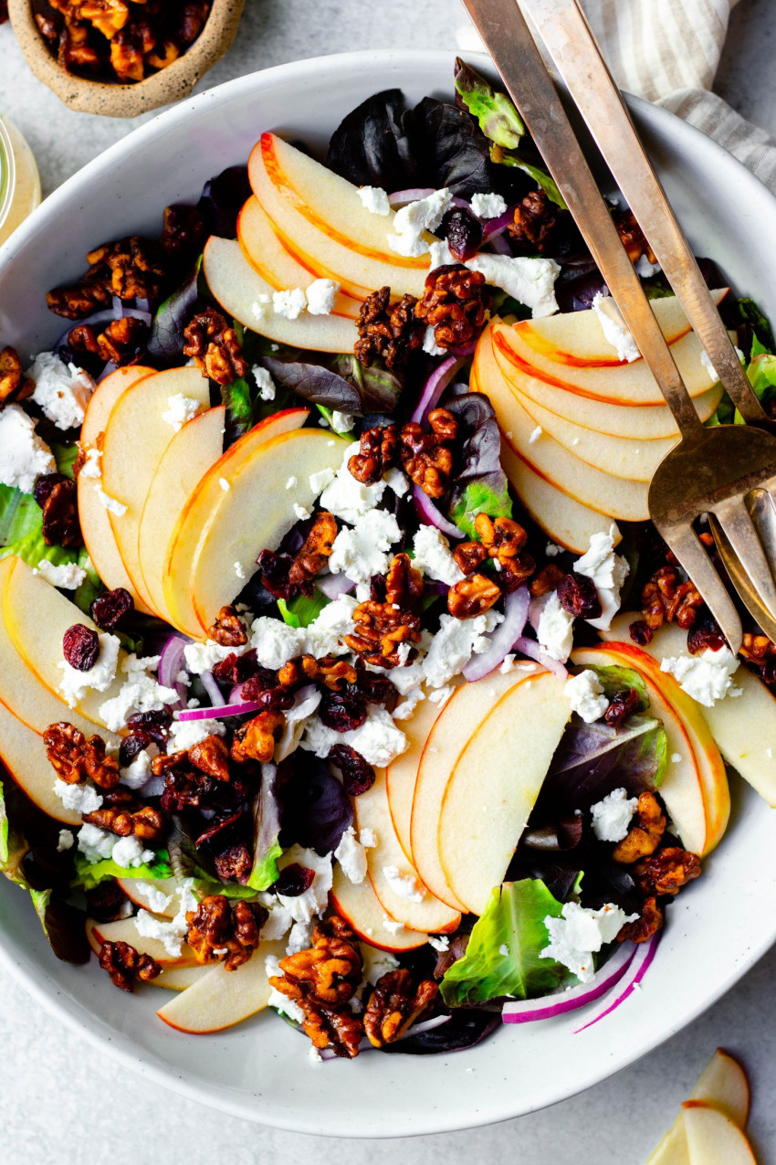 Close up of apple cranberry walnut salad in a bowl with gold serving spoons
