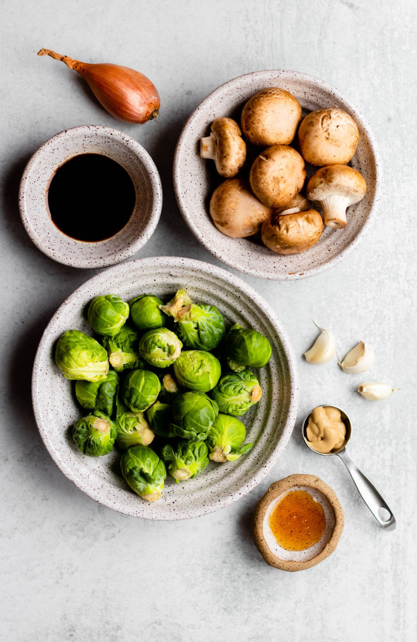 Ingredients for sauteed brussels sprouts and mushrooms measured out on grey backdrop
