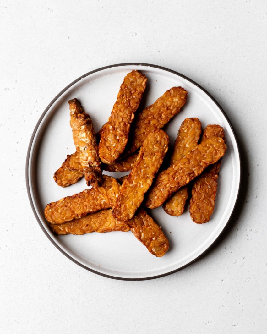 Plate of cooked tempeh strips on a grey backdrop