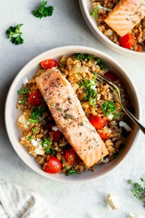 Bowl with salmon and farro with ingredients surrounding on a grey backdrop