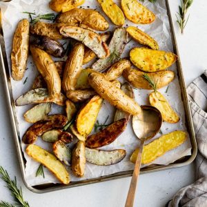 Baking tray of roasted fingerling potatoes with rosemary and a golden serving spoon