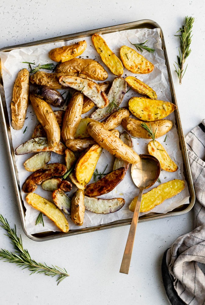 Baking tray of roasted fingerling potatoes with rosemary and a golden serving spoon