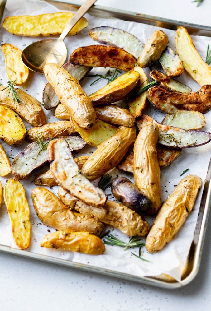 Close up of a baking tray with roasted fingerling potatoes and fresh rosemary