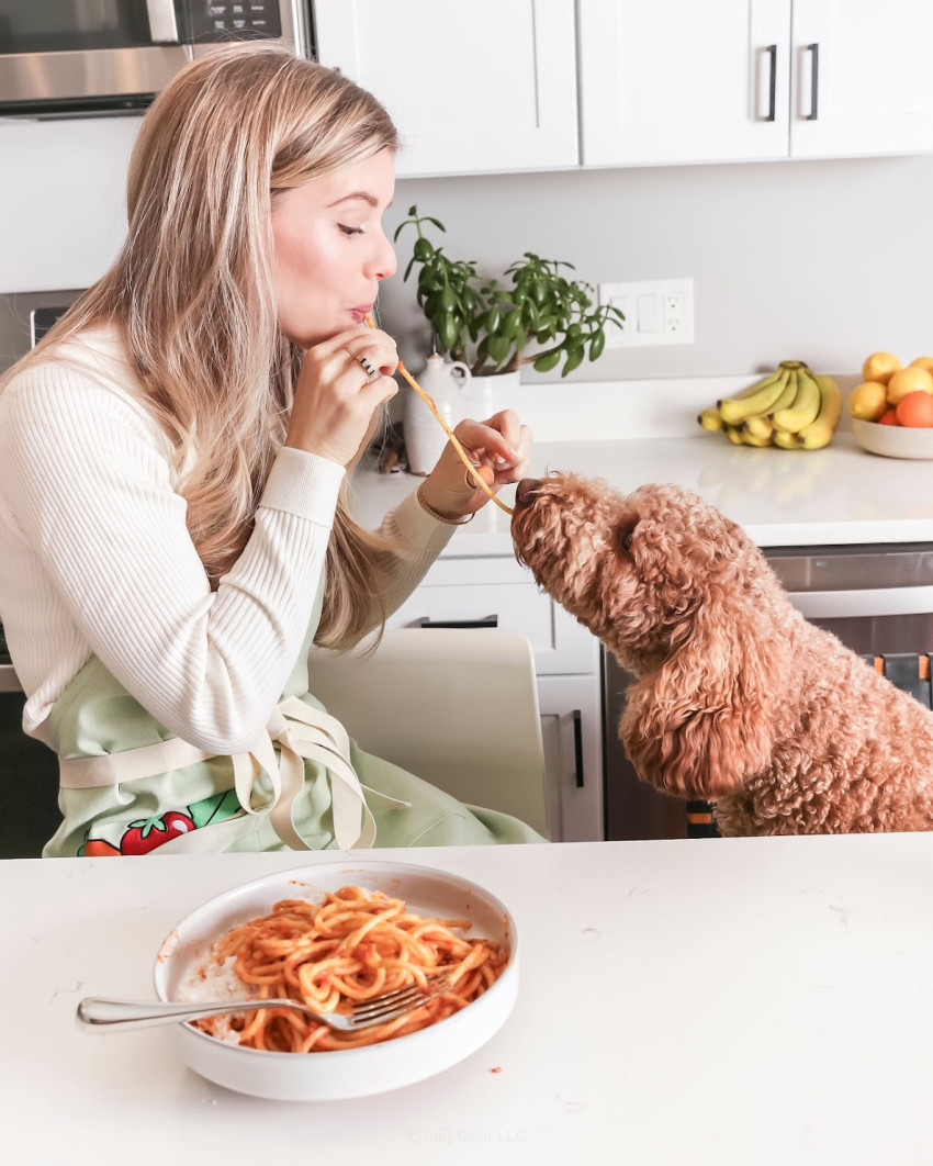 blonde woman and red poodle sharing a plate of pasta