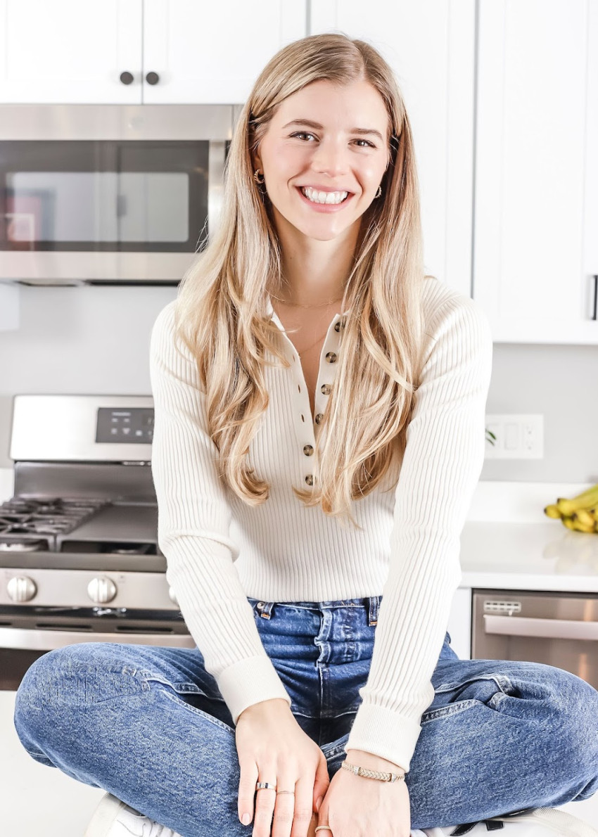 Blonde woman sitting on a kitchen counter wearing a white top and jeans