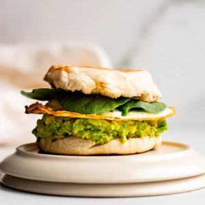 Fried egg sandwich with mashed avocado on a toasted english muffin with spinach leaves