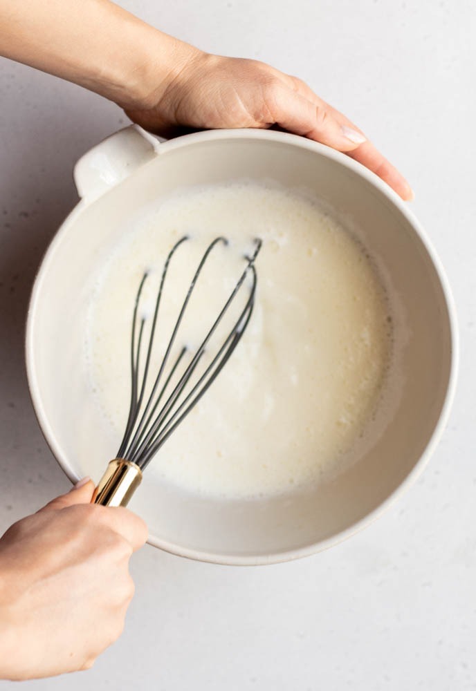 Hand whisking up egg whites in a white mixing bowl